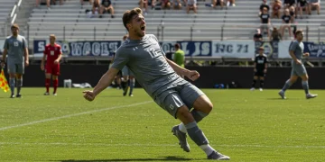 Male collegiate soccer player celebrating a goal on the field.