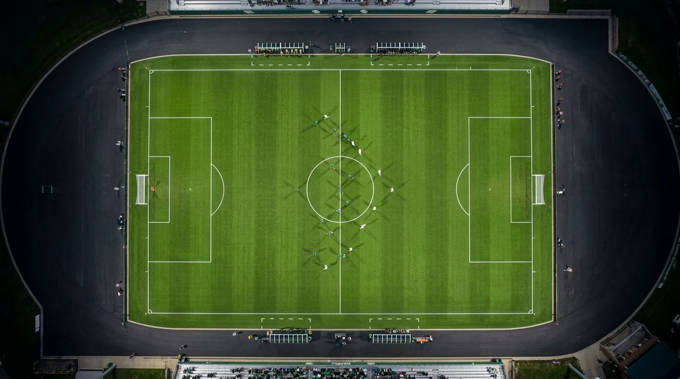 Vue aérienne d'un terrain de soccer universitaire vert vif pendant un match, des joueurs en uniformes verts et blancs formant des motifs stratégiques sur le gazon impeccable sous des lumières douces.